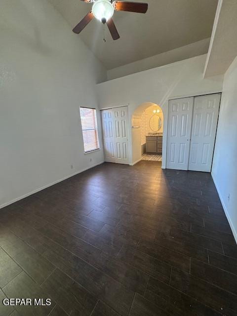 unfurnished bedroom featuring ceiling fan, arched walkways, baseboards, high vaulted ceiling, and dark wood-style floors