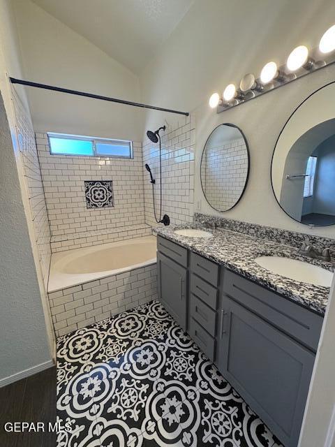 full bathroom featuring double vanity, a sink, tiled shower / bath, and vaulted ceiling