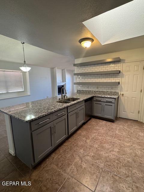 kitchen with stainless steel dishwasher, a peninsula, dark stone counters, gray cabinets, and a sink