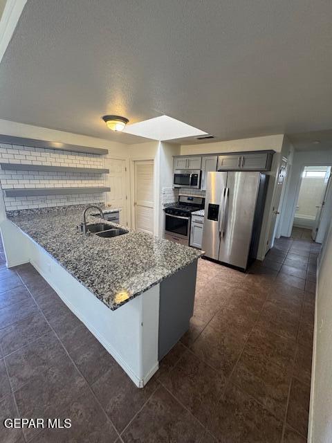kitchen with appliances with stainless steel finishes, a sink, gray cabinetry, a peninsula, and stone counters
