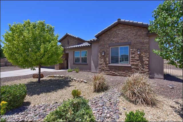 view of front of property with stucco siding, a tiled roof, stone siding, and fence