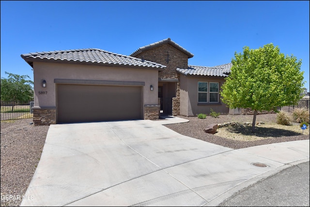 mediterranean / spanish home featuring a garage, fence, stone siding, a tiled roof, and driveway