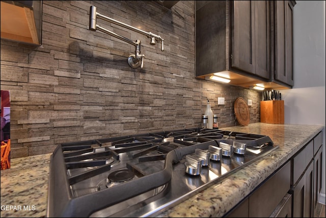 kitchen featuring dark brown cabinets, light stone countertops, decorative backsplash, and stainless steel gas stovetop