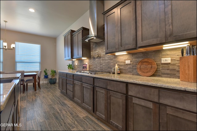 kitchen with dark brown cabinets, a chandelier, wall chimney exhaust hood, baseboards, and tasteful backsplash