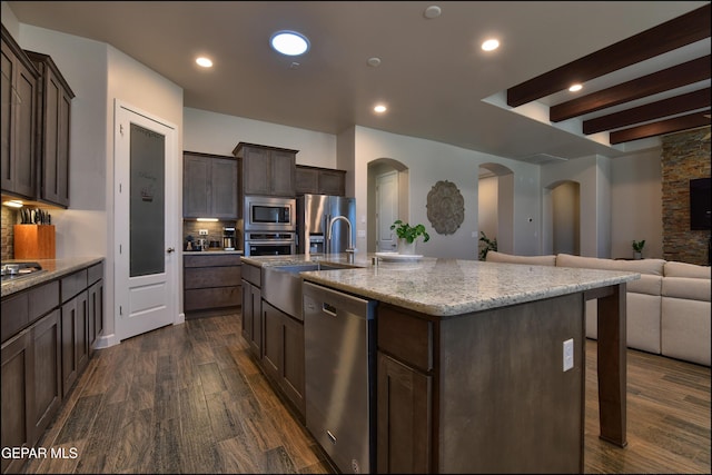 kitchen featuring a sink, arched walkways, stainless steel appliances, open floor plan, and dark wood-style floors