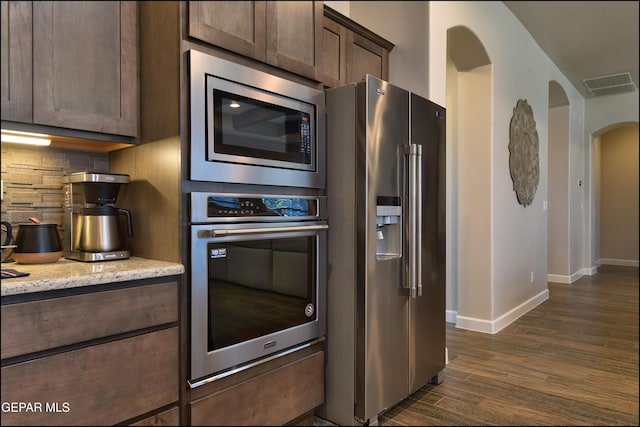 kitchen with dark wood-style flooring, arched walkways, stainless steel appliances, baseboards, and tasteful backsplash