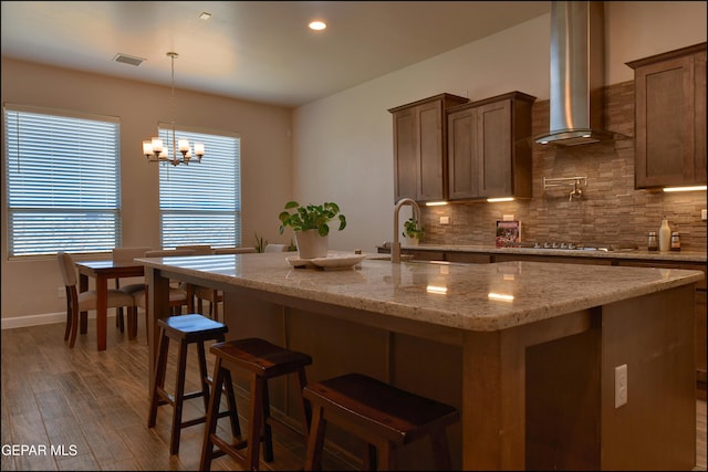 kitchen featuring a sink, a chandelier, wall chimney exhaust hood, decorative backsplash, and cooktop
