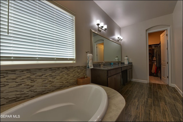 full bathroom featuring vanity, a walk in closet, a bath, and wood finished floors