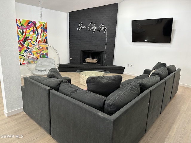 living area with baseboards, a brick fireplace, light wood-style flooring, and lofted ceiling