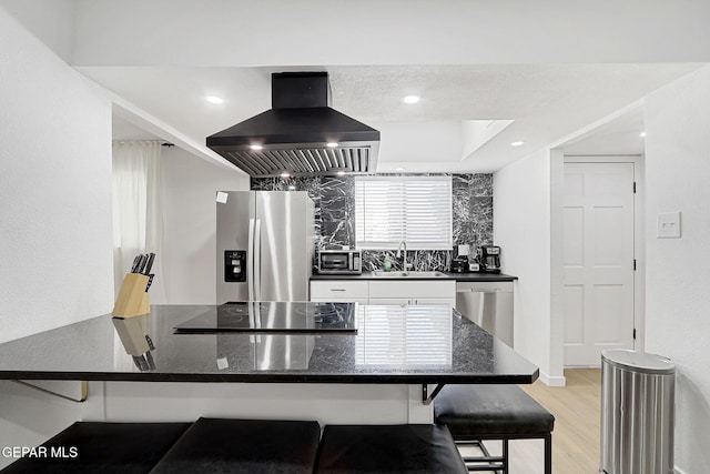 kitchen featuring island exhaust hood, appliances with stainless steel finishes, a sink, white cabinets, and a peninsula