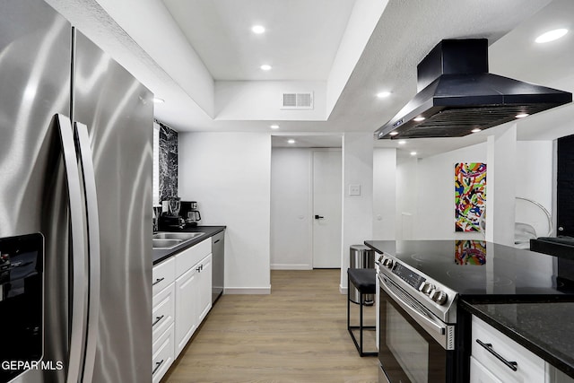 kitchen featuring wall chimney range hood, visible vents, appliances with stainless steel finishes, light wood finished floors, and white cabinetry