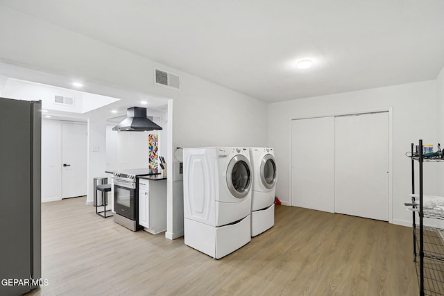 laundry area with laundry area, washing machine and dryer, light wood-style flooring, and visible vents