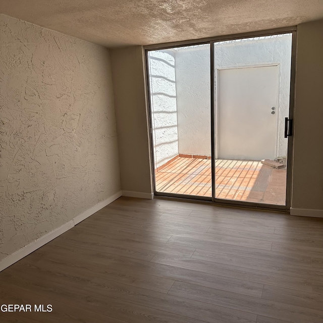 spare room with baseboards, a textured ceiling, a textured wall, and wood finished floors