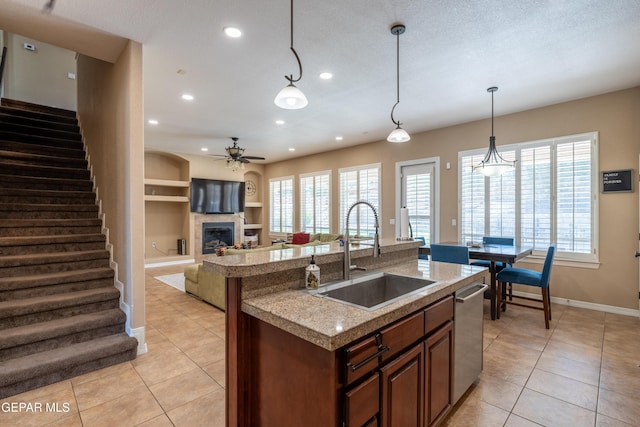 kitchen with a sink, ceiling fan, a glass covered fireplace, and light tile patterned flooring