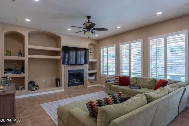 tiled living room with a ceiling fan, built in shelves, a tile fireplace, baseboards, and recessed lighting