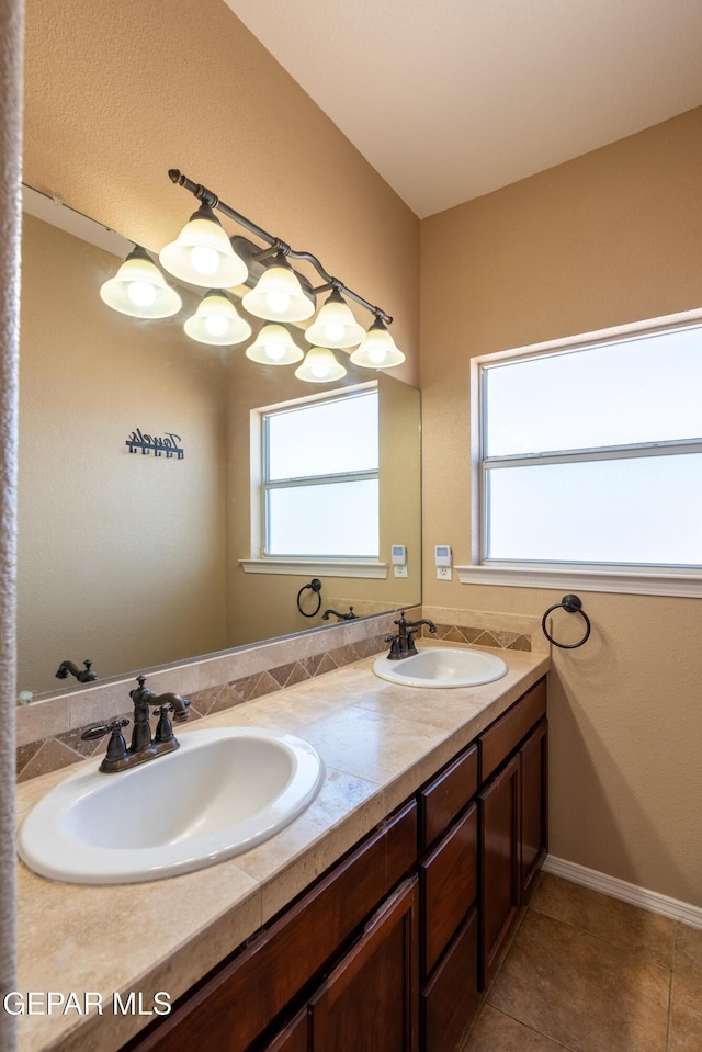 bathroom with baseboards, double vanity, tile patterned floors, and a sink