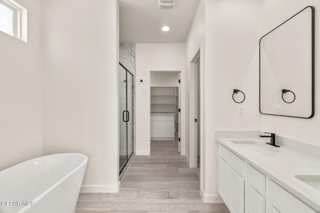 full bath featuring a walk in closet, a shower stall, a sink, baseboards, and a soaking tub
