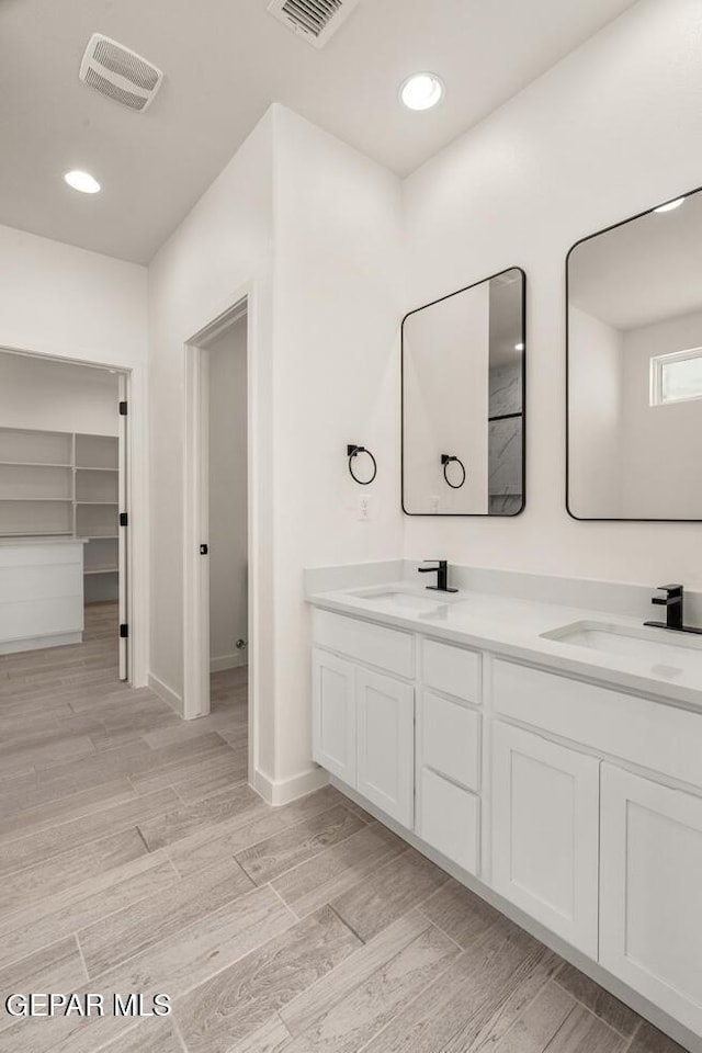 bathroom with a sink, wood finished floors, double vanity, and visible vents