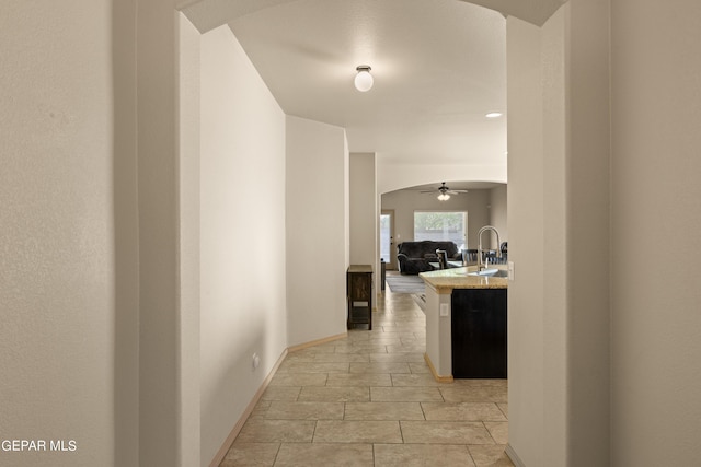 corridor featuring arched walkways, baseboards, and a sink