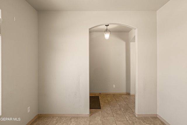 empty room featuring arched walkways, baseboards, and light tile patterned floors