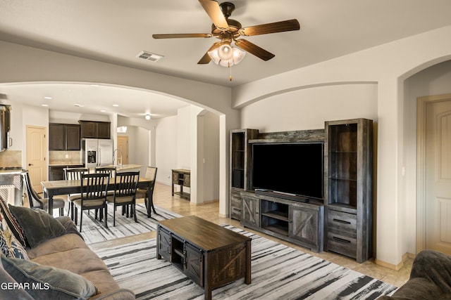 living room featuring a ceiling fan, visible vents, arched walkways, light tile patterned floors, and baseboards