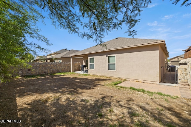 rear view of house featuring fence, a gate, and stucco siding