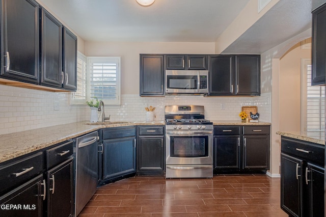 527 Longleaf Pl, El Paso, TX 79928 - kitchen featuring dark wood-style flooring, light stone countertops, appliances with stainless steel finishes, a sink, and arched walkways