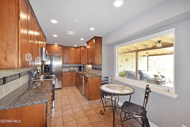 kitchen featuring decorative backsplash, dark stone countertops, visible vents, and brown cabinets
