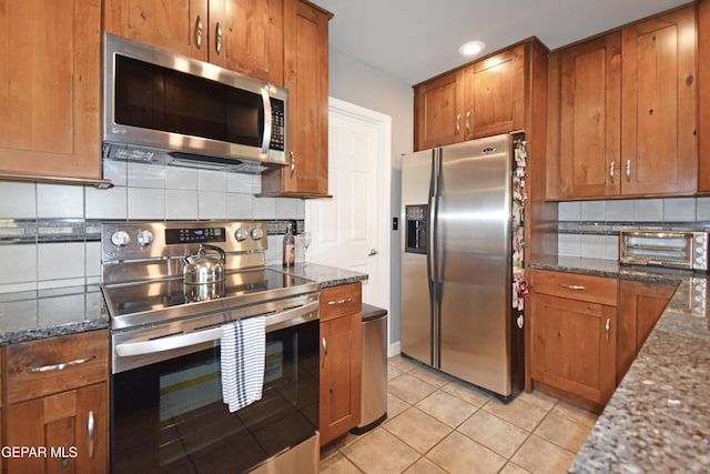 kitchen featuring brown cabinetry, stainless steel appliances, dark stone countertops, a toaster, and decorative backsplash