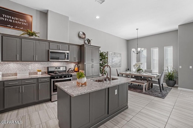 kitchen with backsplash, appliances with stainless steel finishes, light stone countertops, a sink, and gray cabinetry