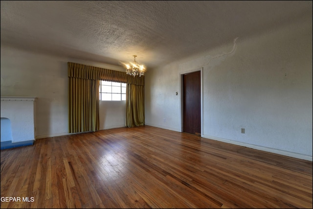 spare room featuring a chandelier, wood finished floors, a textured ceiling, and baseboards