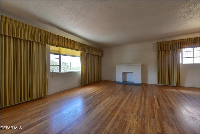 unfurnished living room featuring wood finished floors, healthy amount of natural light, a textured ceiling, and a fireplace with raised hearth