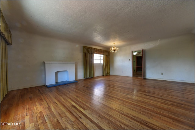 unfurnished living room with a chandelier, a textured ceiling, hardwood / wood-style floors, a fireplace, and baseboards