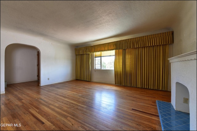 unfurnished living room featuring arched walkways, a textured ceiling, wood finished floors, and a tile fireplace