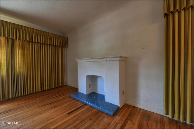 unfurnished living room featuring wood finished floors, baseboards, and a tiled fireplace
