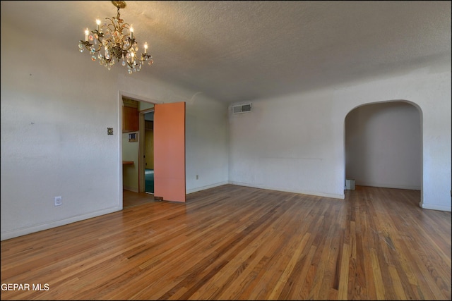 unfurnished room with arched walkways, wood finished floors, a chandelier, a textured ceiling, and baseboards