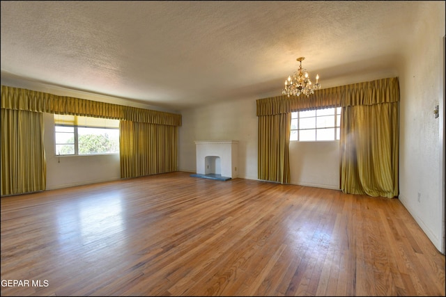 unfurnished living room with a chandelier, light wood-type flooring, a textured ceiling, and a fireplace