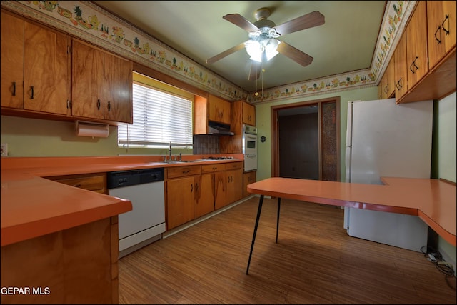 kitchen with white appliances, brown cabinets, a sink, light wood-style floors, and under cabinet range hood
