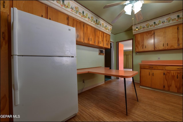 kitchen with freestanding refrigerator, a ceiling fan, brown cabinetry, and light wood-style flooring