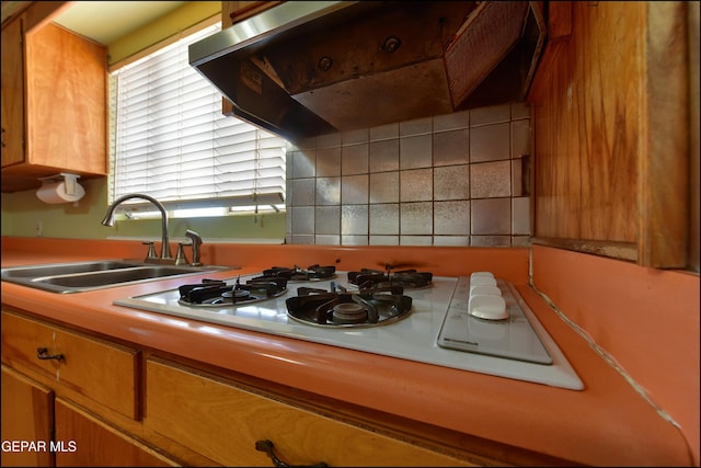kitchen with a sink, under cabinet range hood, light countertops, brown cabinetry, and white gas cooktop