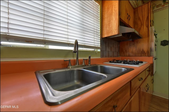 kitchen featuring a sink, white gas cooktop, brown cabinets, and under cabinet range hood