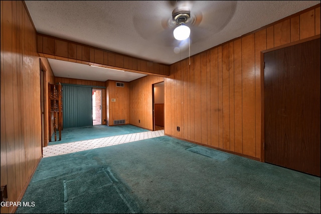 spare room with carpet floors, ceiling fan, wood walls, and a textured ceiling
