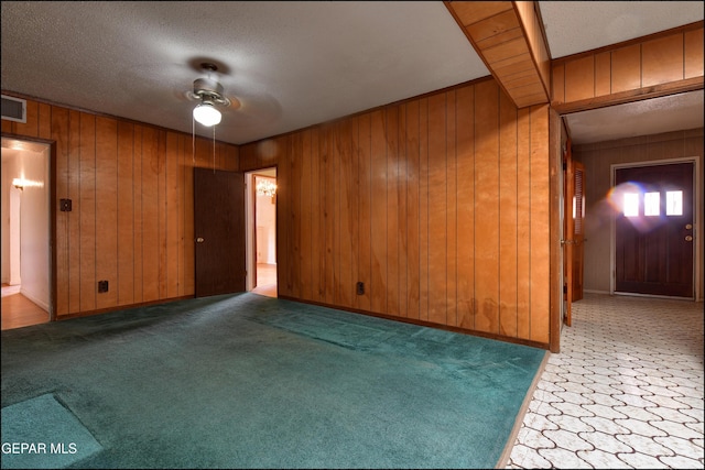 spare room featuring a ceiling fan, wooden walls, a textured ceiling, and carpet flooring