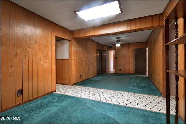carpeted empty room featuring wood walls, a ceiling fan, and a textured ceiling