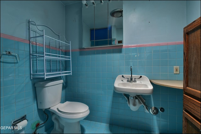 half bathroom featuring tile walls, toilet, and a wainscoted wall