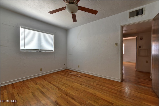 empty room with wood finished floors, a ceiling fan, baseboards, and a textured ceiling