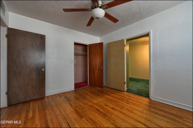 unfurnished bedroom featuring wood-type flooring, a textured wall, a closet, ceiling fan, and baseboards