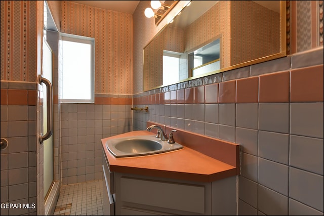 full bath featuring wallpapered walls, tile walls, a stall shower, a wainscoted wall, and vanity