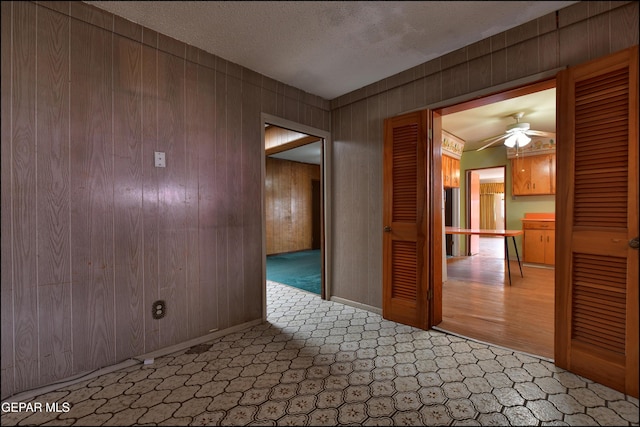 empty room featuring a ceiling fan, baseboards, wooden walls, a textured ceiling, and carpet