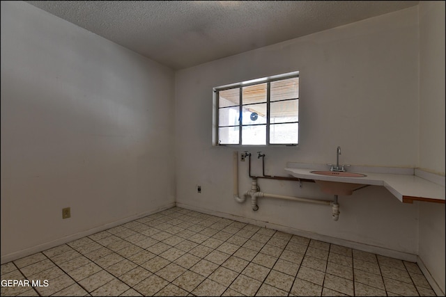 empty room with a sink, a textured ceiling, and baseboards